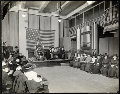 People in an Auditorium at the New York Association for the Blind with Christmas Tree and People Possibly Performing a Skit on Stage with Organ by Byron Company